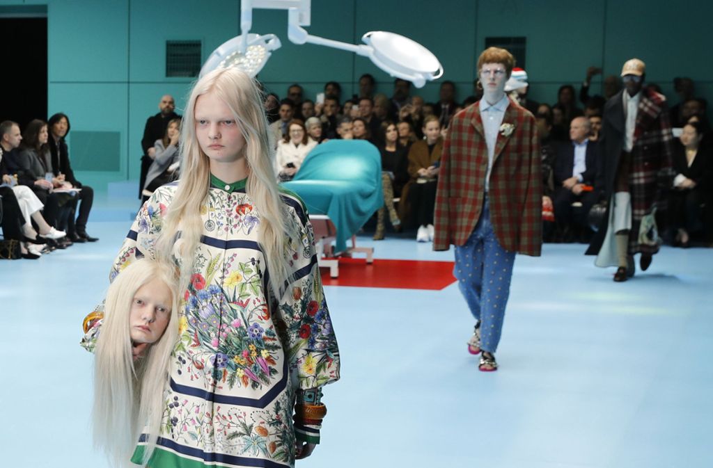 Ein Model trägt eine Kreation und einen Papp-Kopf unter dem Arm der Damen-Kollektion von Gucci.