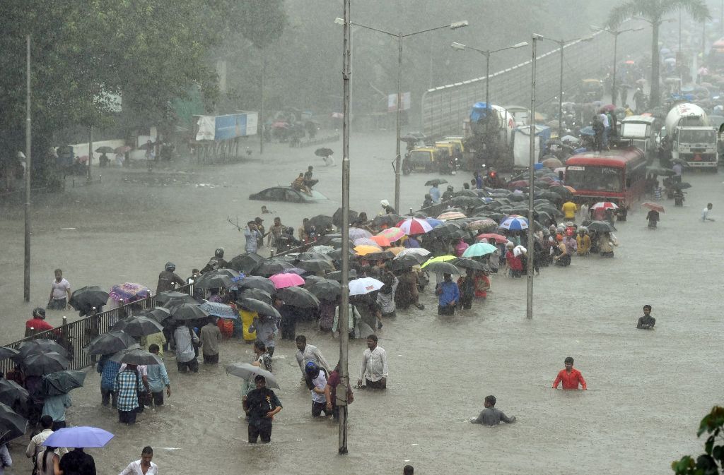 Menschen waten in Mumbai (Indien) über eine überflutete Straße. Heftige Regenfälle haben Teile der Stadt lahmgelegt.