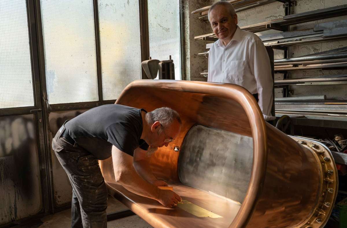 Der Künstler Edgar Harwardt beobachtet, wie Bernd Höger das Innere der Kupferbadewanne vergoldet. Dabei werden dünne Goldplättchen mit einem Pinsel aufgetragen.