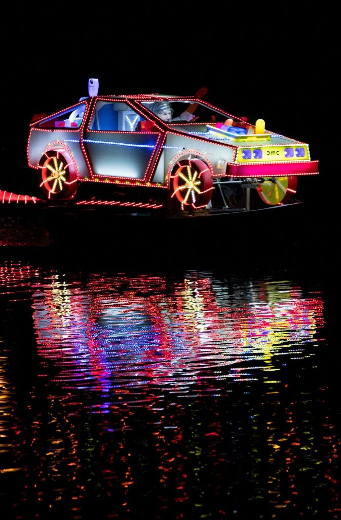 In der Nacht wirkt es fast so, als würde ein knallbuntes Auto über den Fluss fahren. Das dahintersteckende Boot verschwindet in der Dunkelheit.