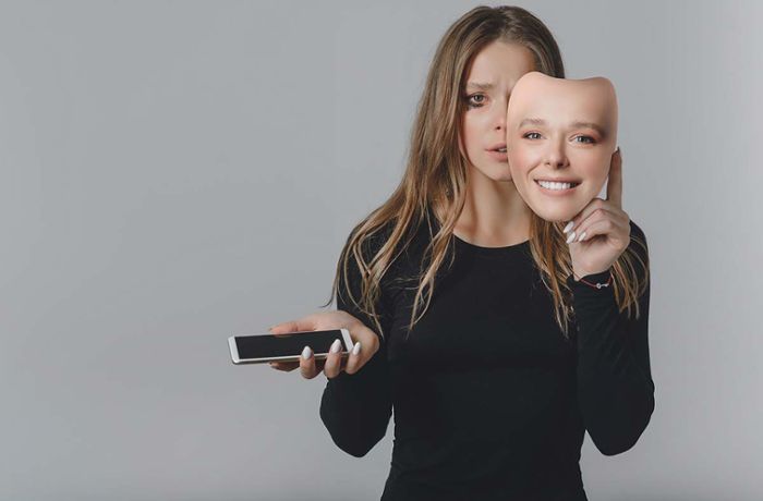 Porträt eines traurigen Mädchens mit einem Smartphone und einer lächelnden Maske in den Händen