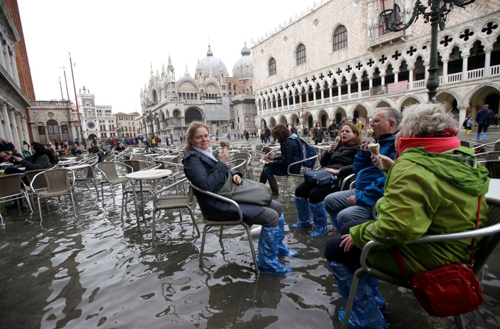 In Venedig essen Touristen ein Eis auf dem überfluteten Markusplatz.