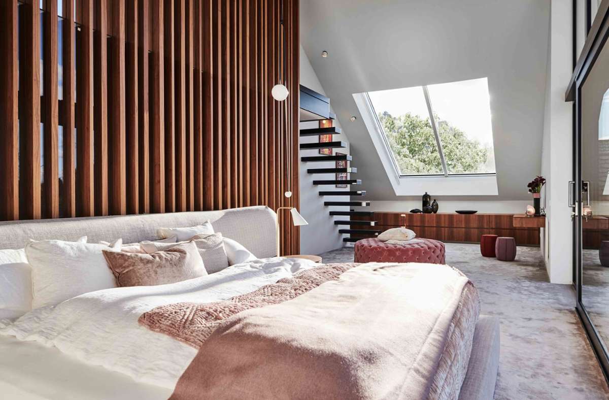 Anja Pangerl von Blocher Partners aus Stuttgart gestaltete ein Einfamilienhaus in Süddeutschland um. Blick in den Schlafraum. Im Obergeschoss schafft die Lamellenkonstruktion aus Nussbaumholz eine schöne Kulisse fürs Bett. Ein großes Dachfenster sorgt für Ausblicke.