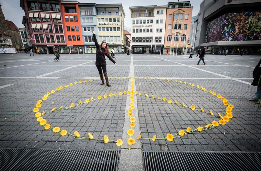 Eine Aktivistin der Deutschen Friedensgesellschaft wirbt 2018 mit Blumen und Peace-Zeichen in Stuttgart für den Frieden.