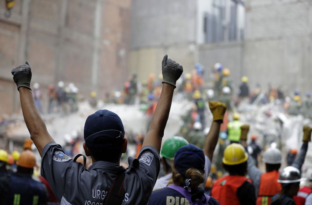 Mit nach oben gestreckten Fäusten stehen freiwillige Helfer in den Trümmern in Mexiko. Das Handzeichen bedeutet den Arbeitern leise zu sein.