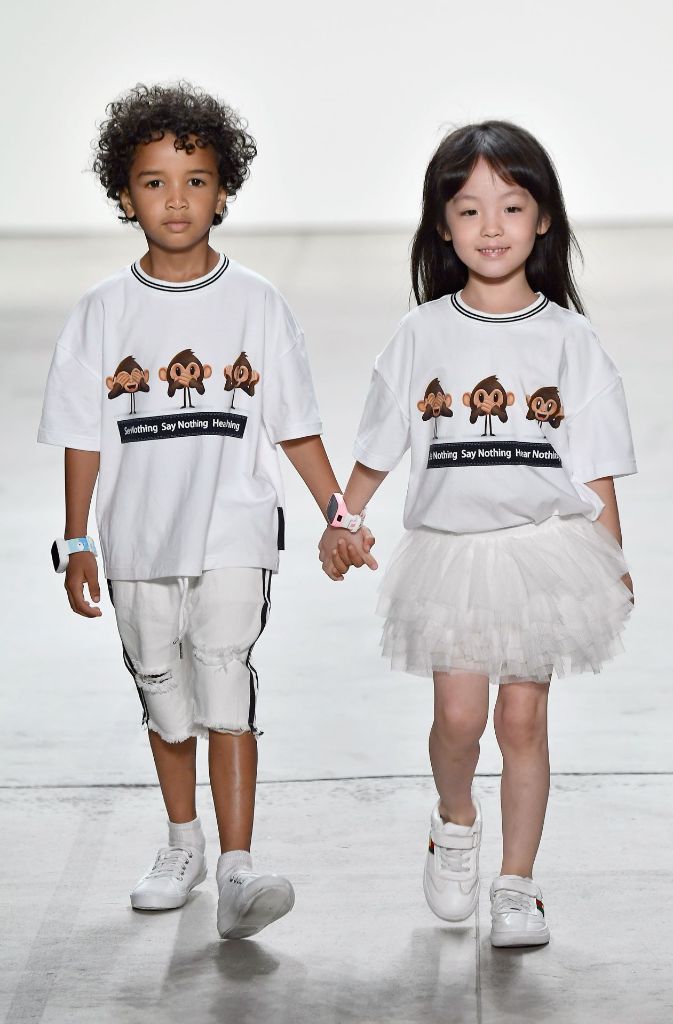 Hand in Hand zeigen die zwei jungen Models ein T-Shirt mit den drei Affen auf dem Laufsteg.