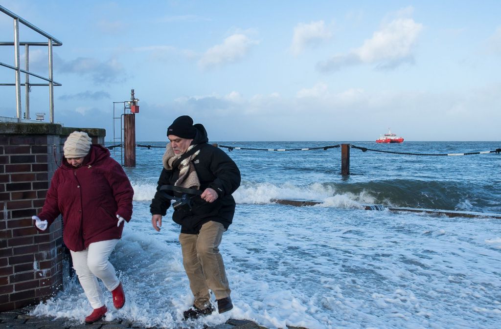 Zwei Weihnachtsspaziergänger flüchten in Cuxhaven vor einer herranrollenden Welle.