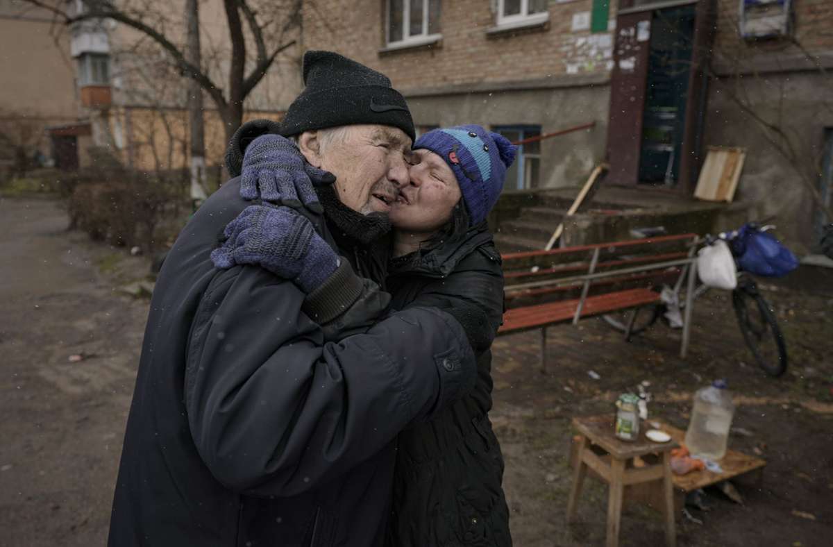 Eine Frau küsst einen Mann, während sie auf einem offenen Feuer vor einem Wohnhaus kocht. Das Haus ist seit Beginn der russischen Invasion in Butscha, Ukraine, ohne Strom, Wasser und Gas.